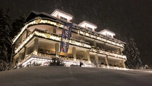A multi-story hotel with balconies, illuminated by warm lights, surrounded by snow. - Boutique Hotel Villa Blu Cortina (Cortina d'Ampezzo)