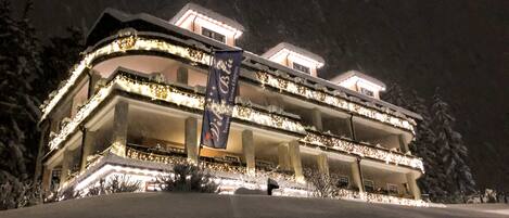 A multi-story hotel with balconies, illuminated by warm lights, surrounded by snow.