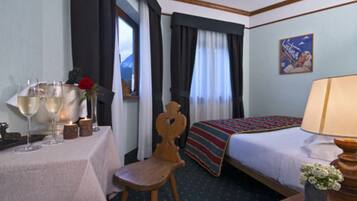 Una camera d'albergo con un letto, un tavolo con bicchieri e un fiore, una sedia, una lampada e un quadro appeso al muro.