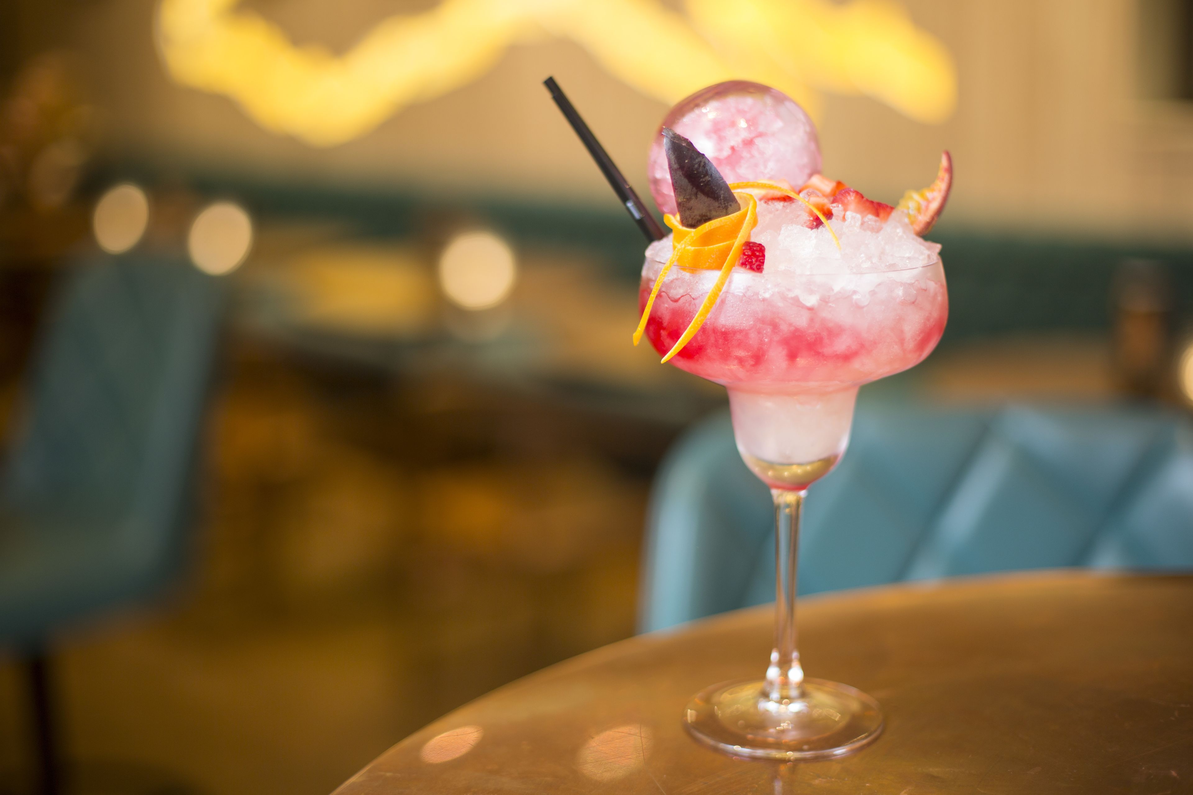 Um cocktail com um guarda-sol decorativo e um canudo, servido num copo sobre uma mesa.