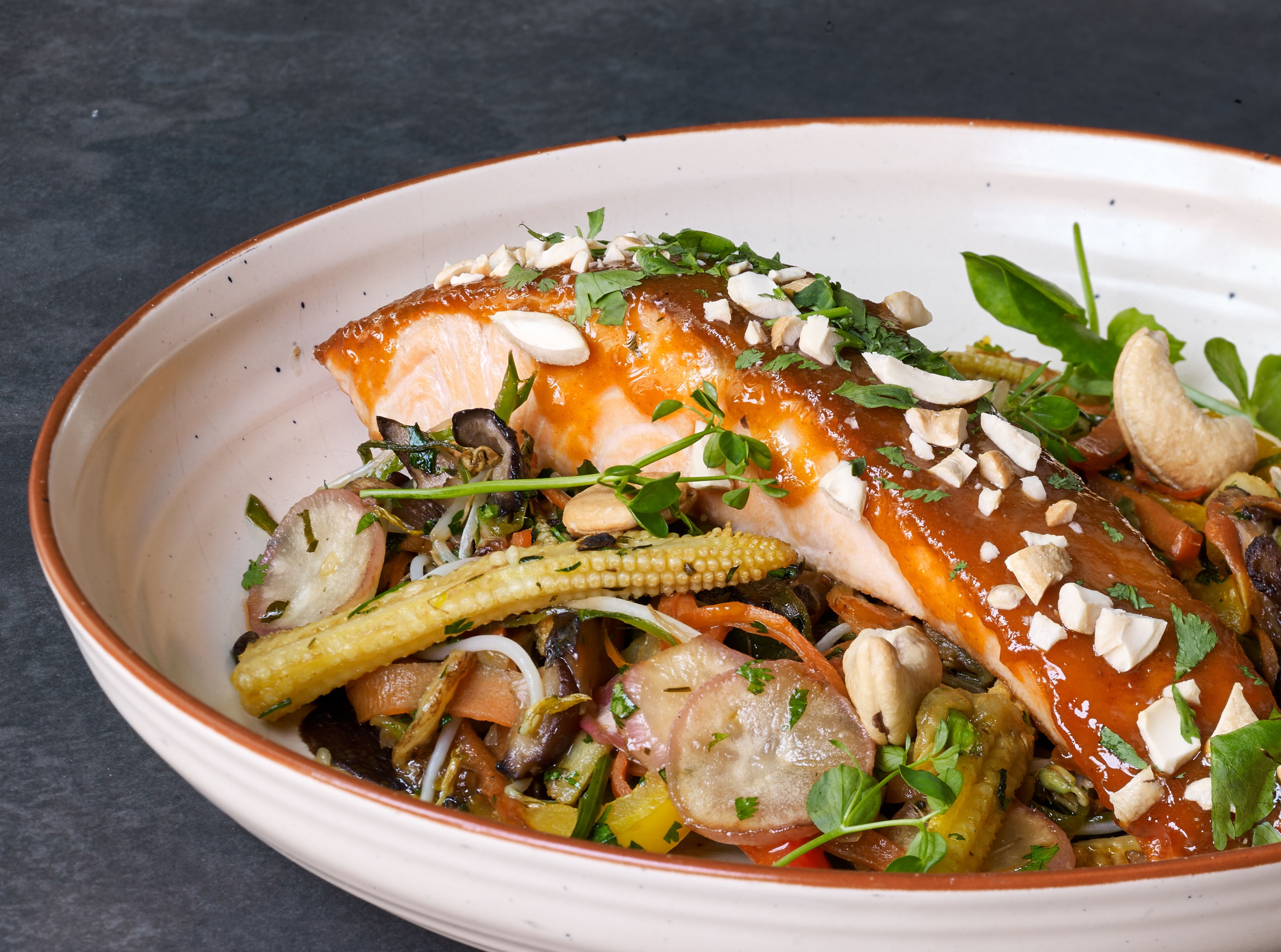 A dish with various vegetables and a piece of fish, garnished with herbs and nuts.