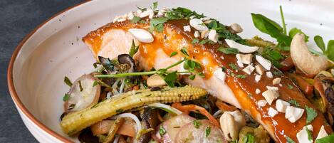 En rätt med olika grönsaker och en bit fisk, garnerad med örter och nötter.