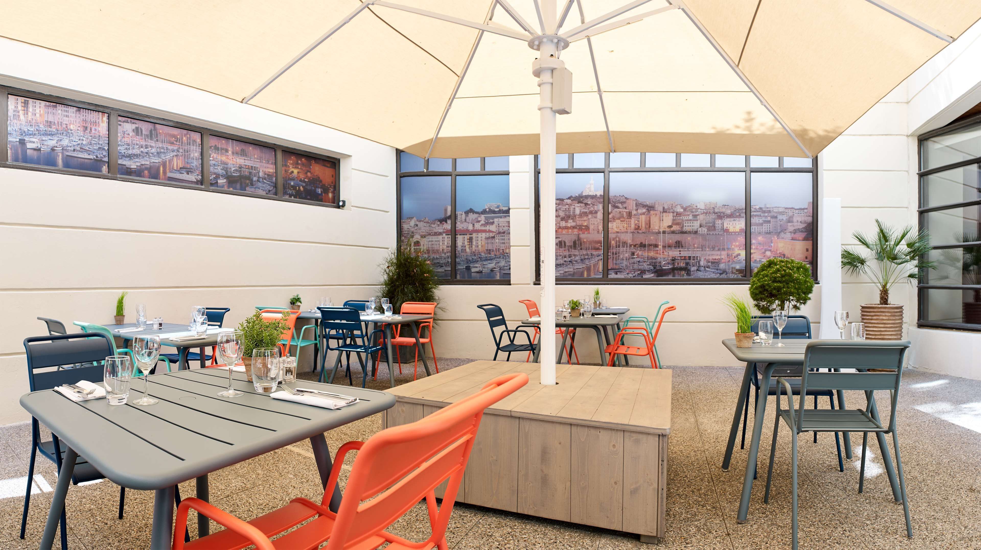 Un espace de restauration en plein air avec plusieurs tables et chaises, de grandes fenêtres offrant une vue sur la ville et des plantes en pot.