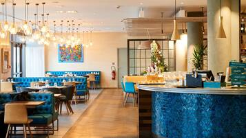 Un restaurante moderno con asientos tapizados en azul, una barra con azulejos azules y lámparas colgantes.