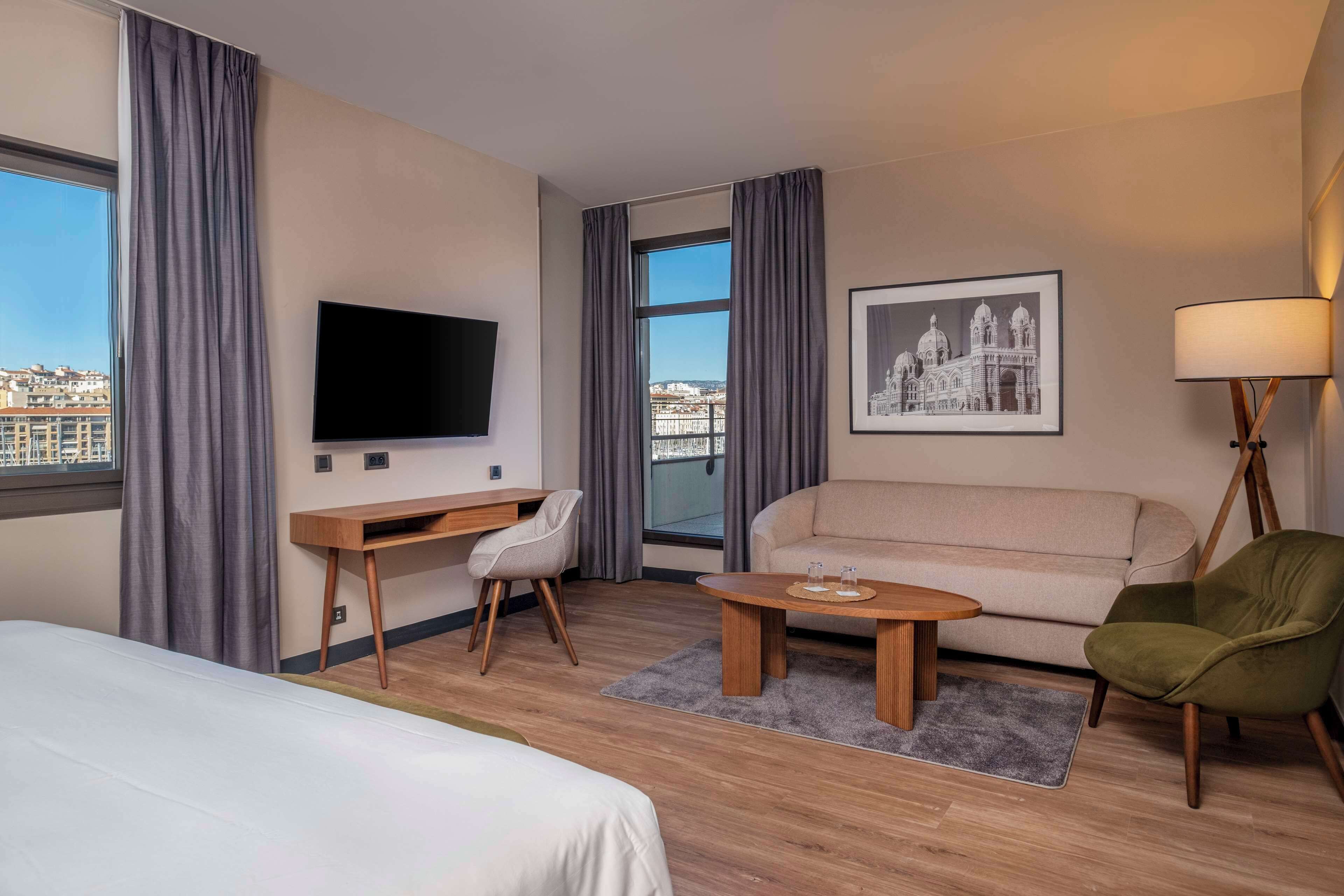 Une chambre d’hôtel équipée d’un lit, d’un bureau, d’un canapé, d’une télévision, d’une lampe et offrant une vue sur le paysage urbain.