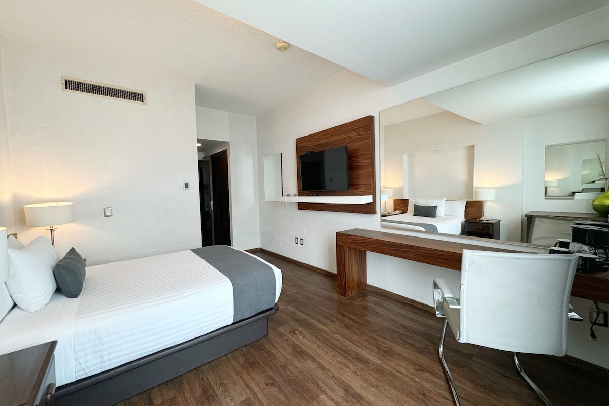 Habitación de hotel con cama, escritorio, silla y televisor fijado a la pared.