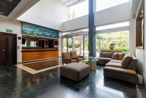 Un hall con mostrador de recepción, zona de estar y un ventanal con vistas a zonas verdes.