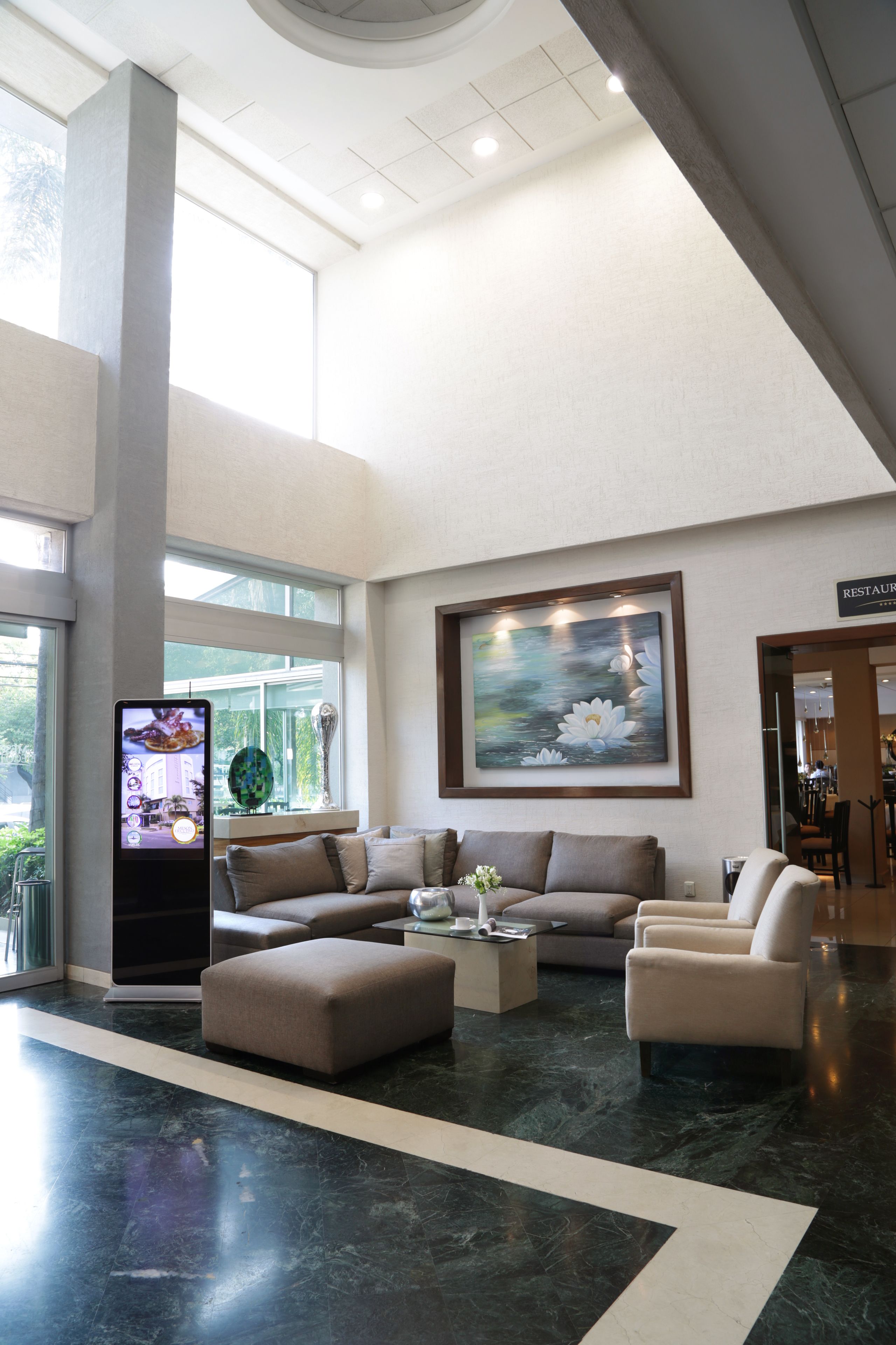 A spacious lobby with a large sofa, a coffee table, and a digital kiosk.