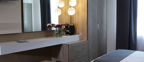 A hotel room with a large bed, a bedside table, a mirror, a vanity with a mirror, a dresser, and a television mounted on the wall.