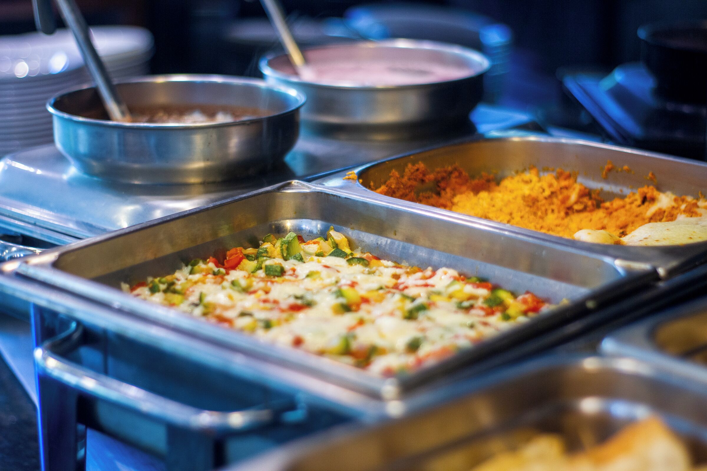 Un buffet con diversi piatti, tra cui una casseruola con verdure e formaggio, un piatto a base di riso e una zuppa.