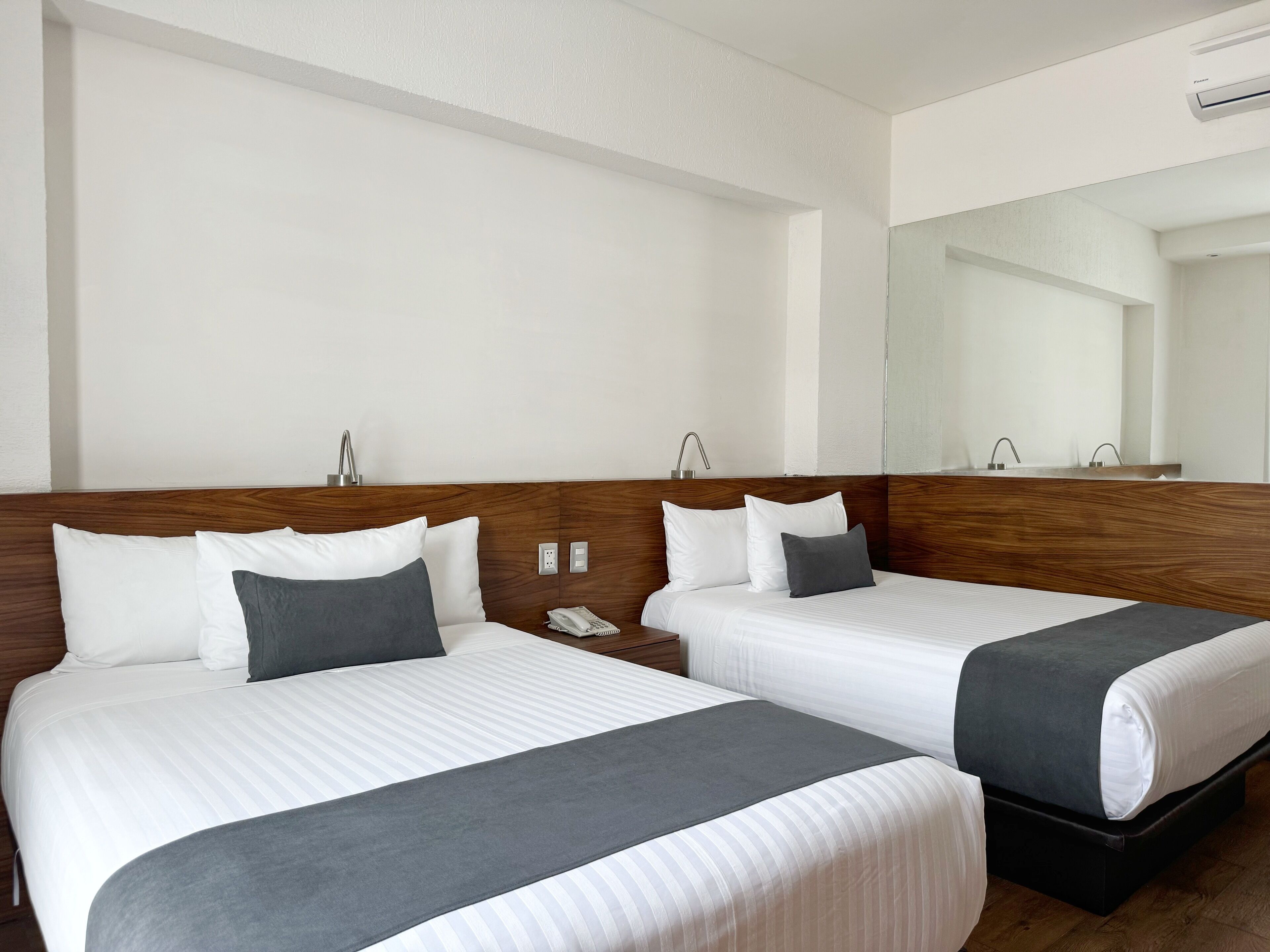 A hotel room with two beds, a wooden headboard, a mirror, and a phone on the nightstand.