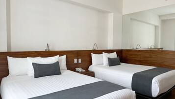 A hotel room with two beds, a wooden headboard, a mirror, and a phone on the nightstand.