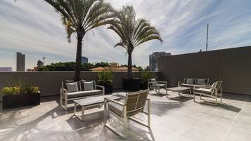A rooftop terrace with outdoor seating, palm trees, and a cityscape view.