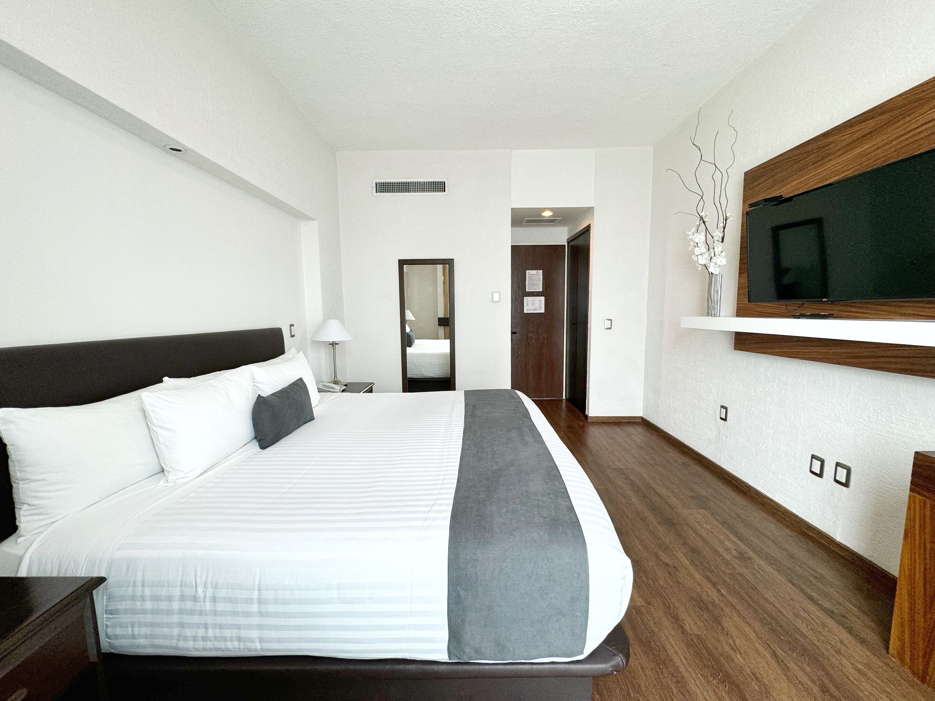 A hotel room with a large bed, a television mounted on the wall, and a wooden floor.