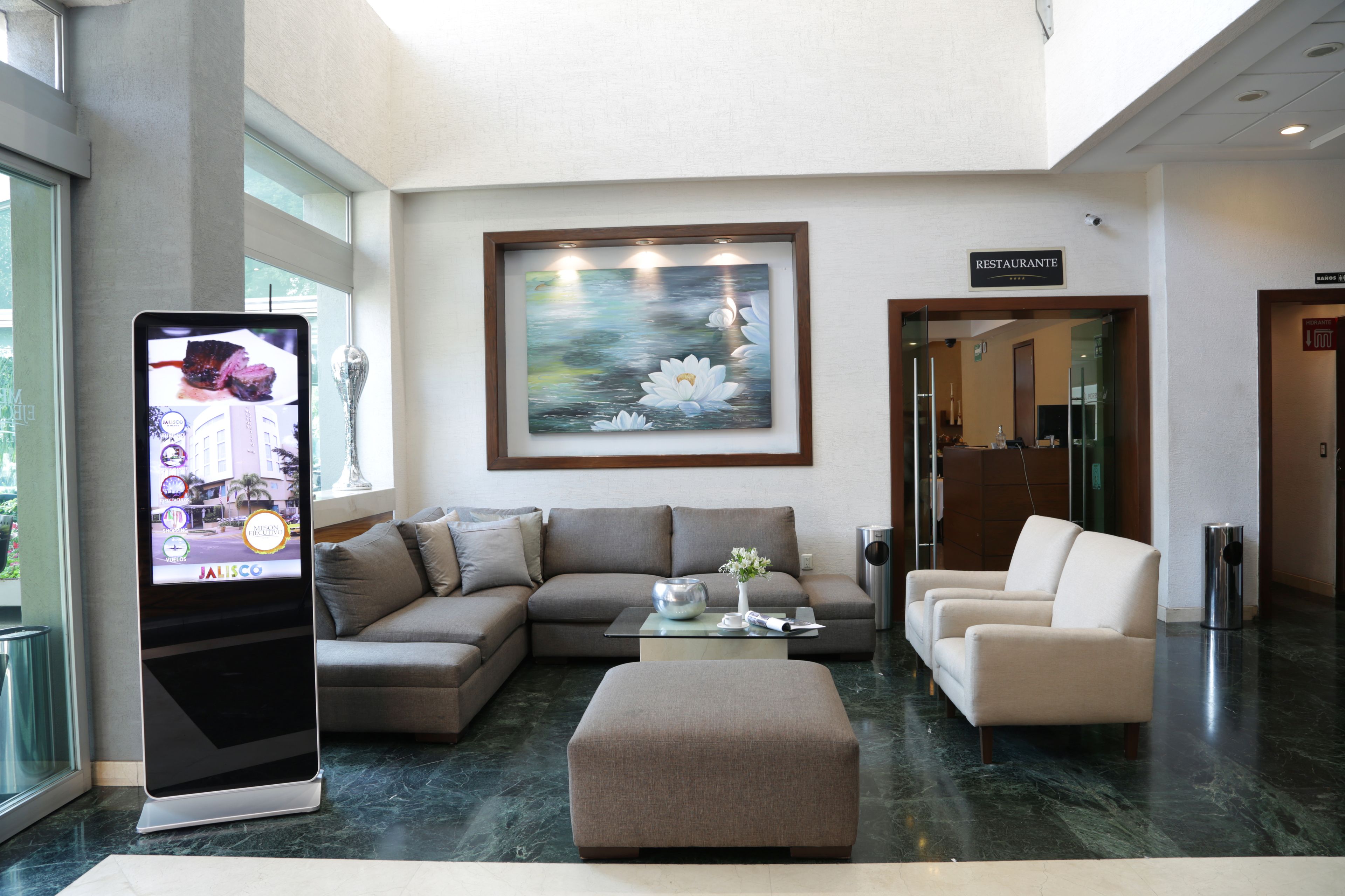 A modern lobby with a sofa, armchairs, a coffee table, and a digital kiosk.