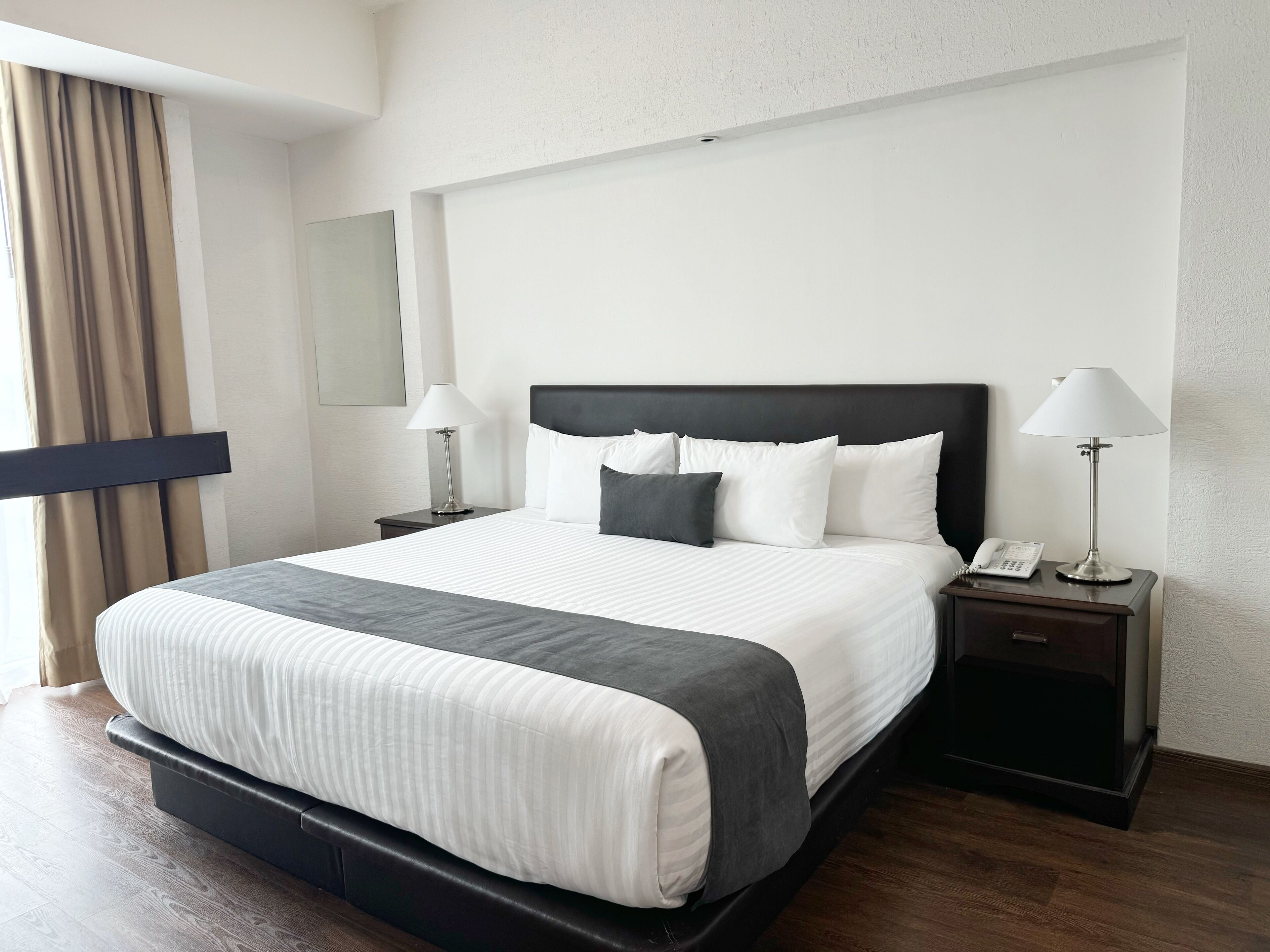 Habitación de hotel con una cama grande, dos mesitas de noche, una lámpara y un teléfono.