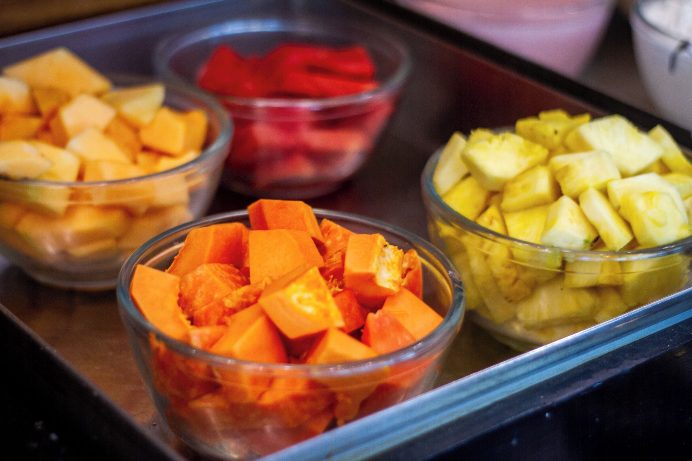 Una bandeja con tazones de frutas cortadas en cubos.