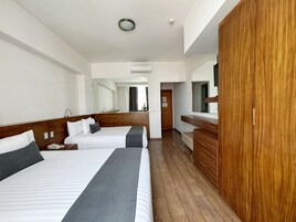 Una habitación de hotel con dos camas, un armario de madera, un espejo y un equipo de aire acondicionado.