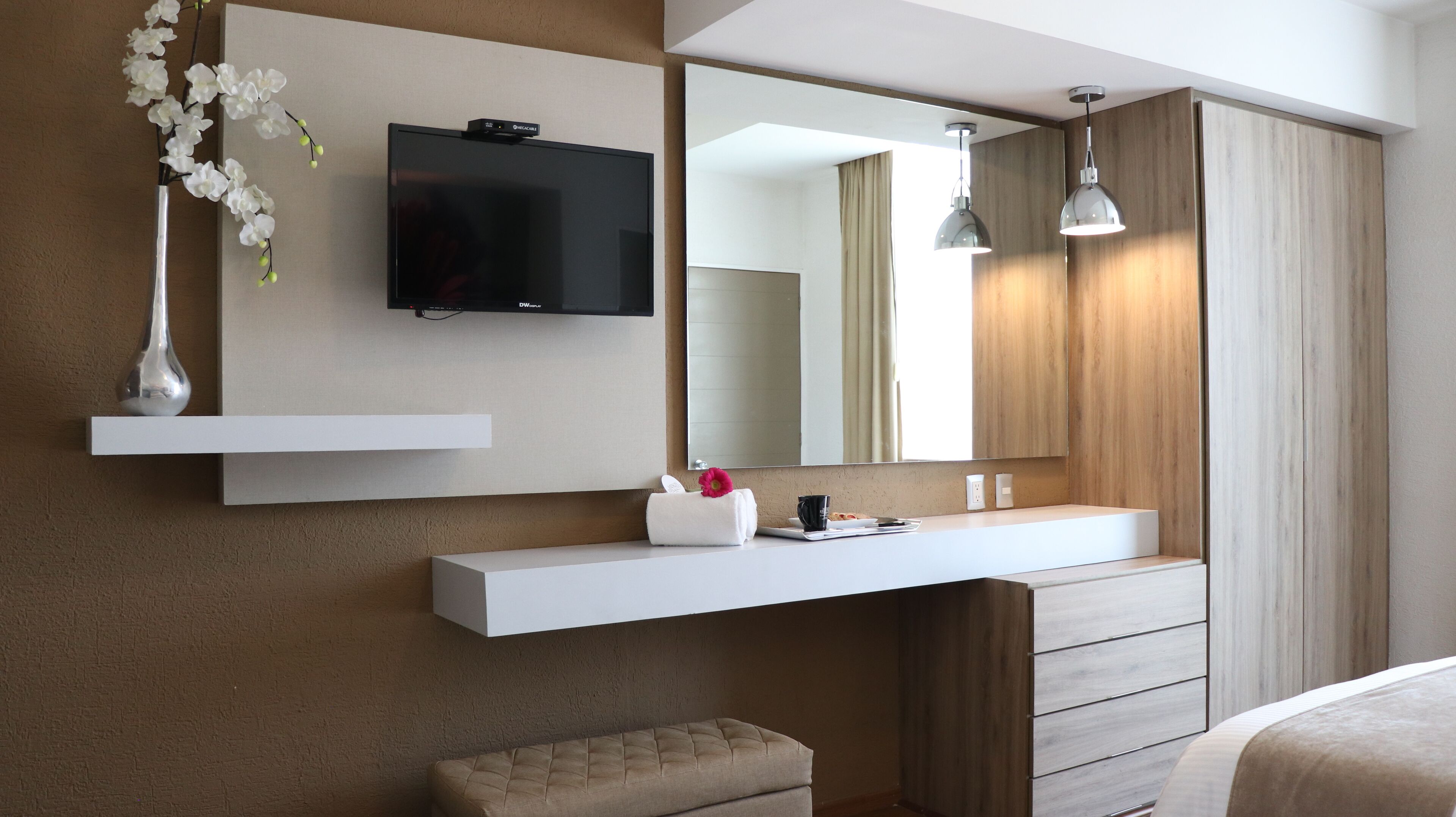 Une salle de bain moderne avec un grand miroir, un téléviseur à écran plat, une commode avec une serviette et un banc.