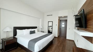 A modern hotel room with a large bed, bedside tables, a flat-screen TV mounted on the wall, and a wooden floor.