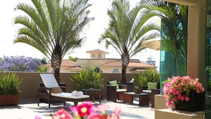 Una terraza en la azotea con mobiliario de mimbre, palmeras y plantas en macetas.