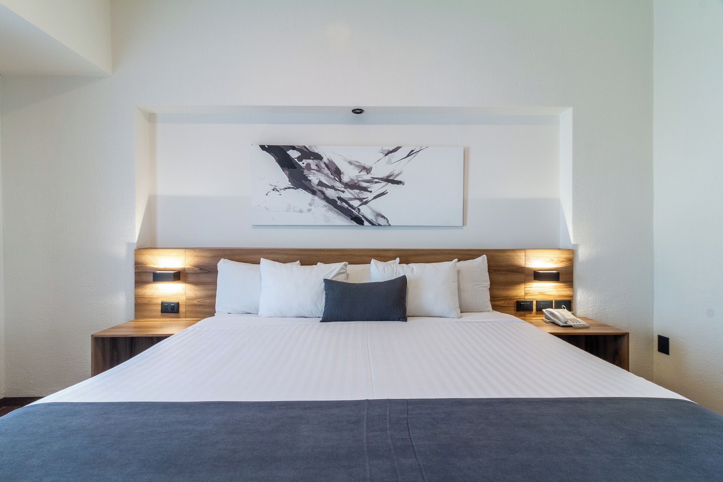 A hotel room with a large bed, two bedside tables with lamps, a wall-mounted artwork, and a telephone on the nightstand.