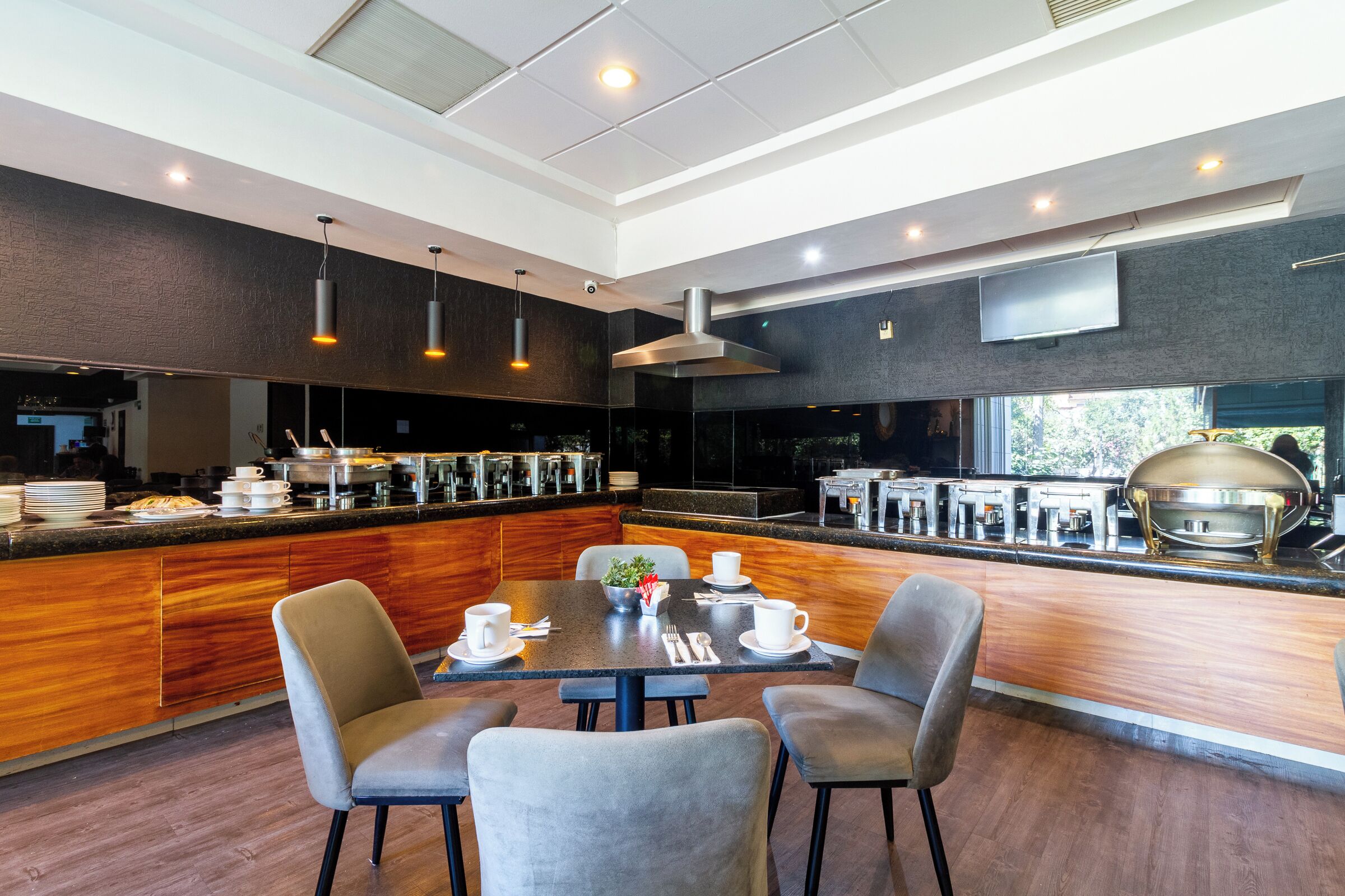 A modern restaurant with a central dining table, bar seating, and a kitchen area with a grill.