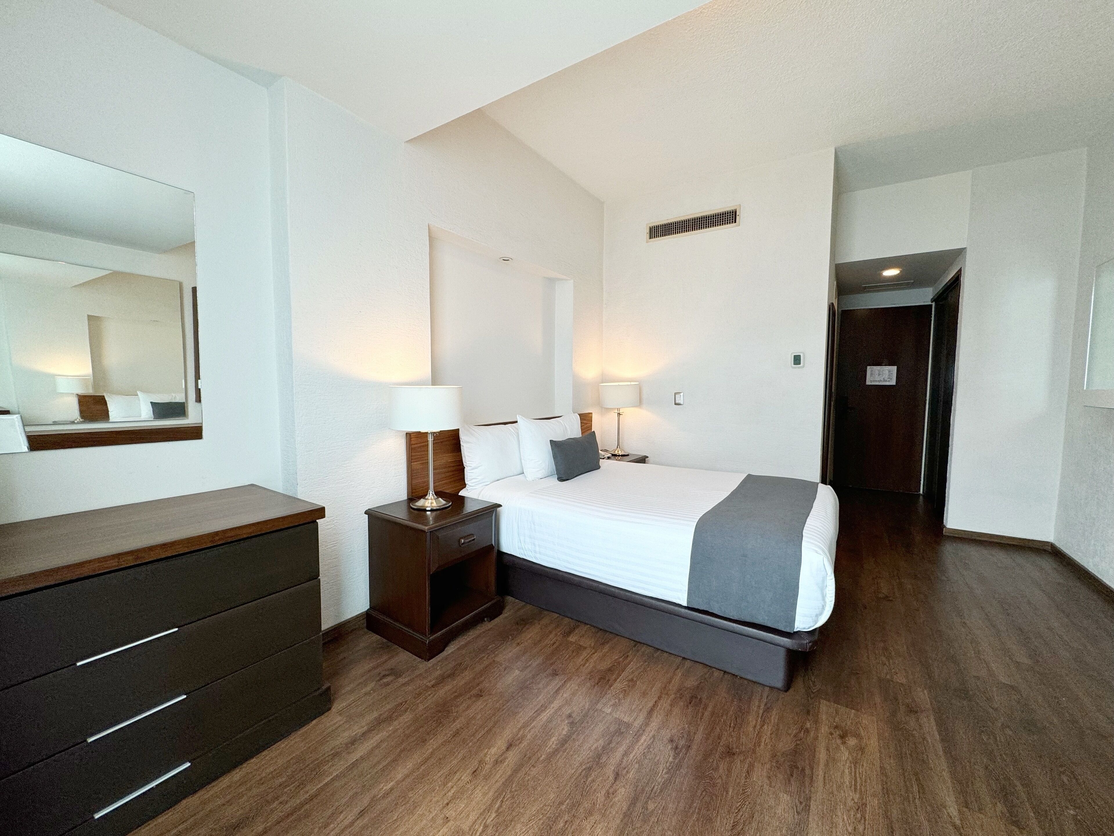 A hotel room with a bed, bedside tables, a dresser, and a mirror.