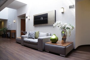 Un moderno vestíbulo de hotel con un sofá gris, un jarrón verde y una obra de arte enmarcada en la pared.
