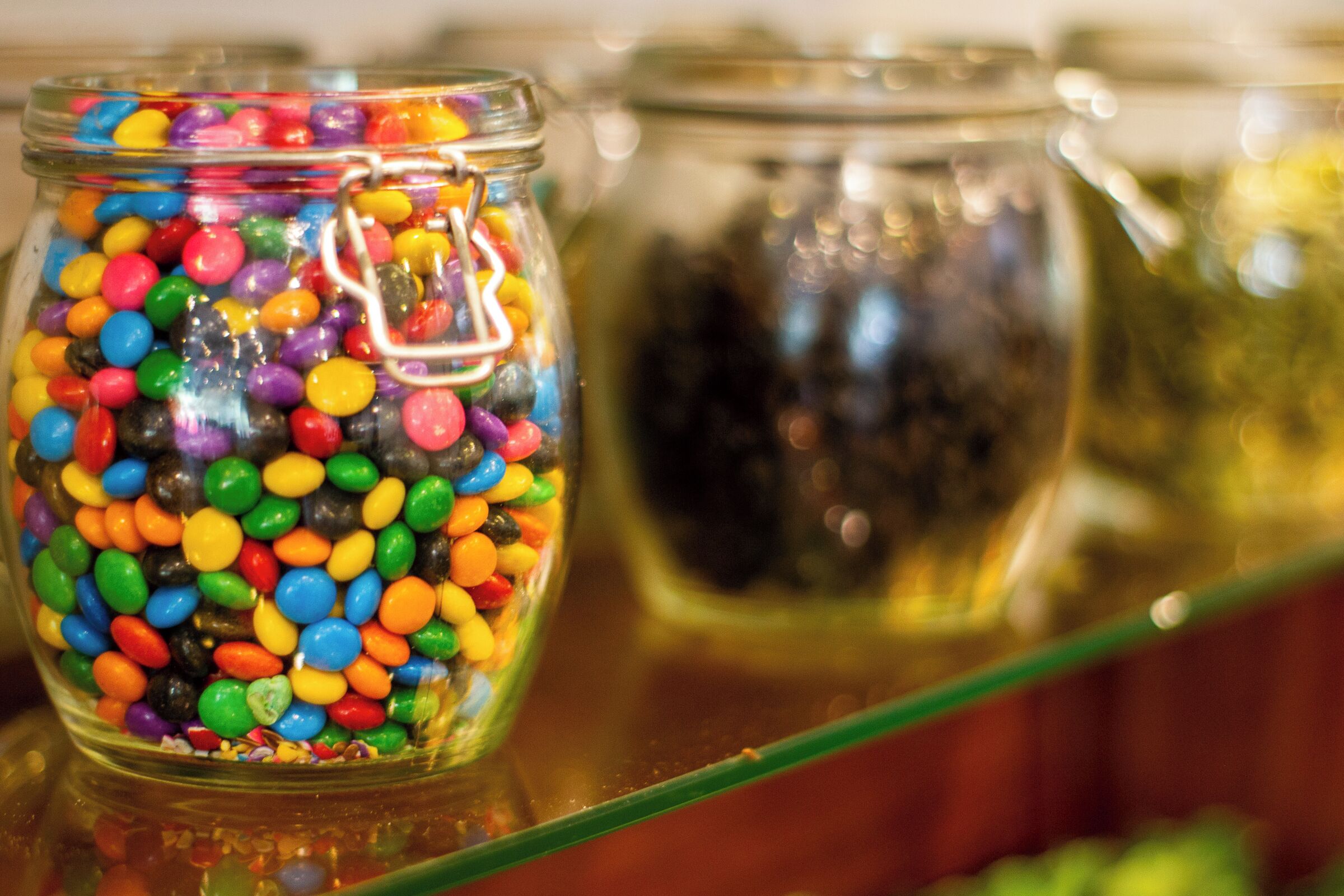 Un tarro de vidrio lleno de caramelos de colores sobre una estantería.