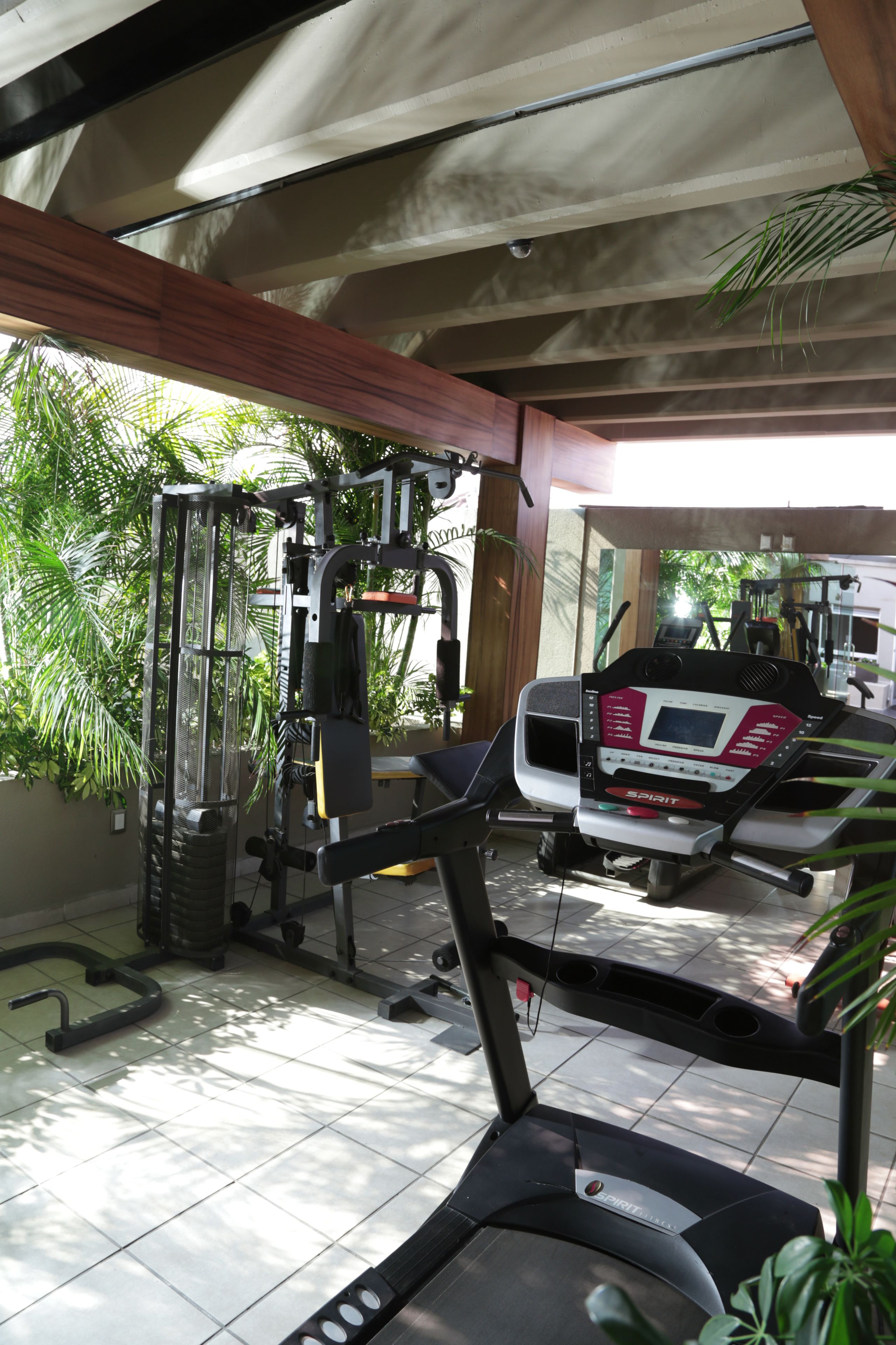 A covered outdoor gym area with exercise equipment, including a treadmill and weight machines, under a roof with natural light.