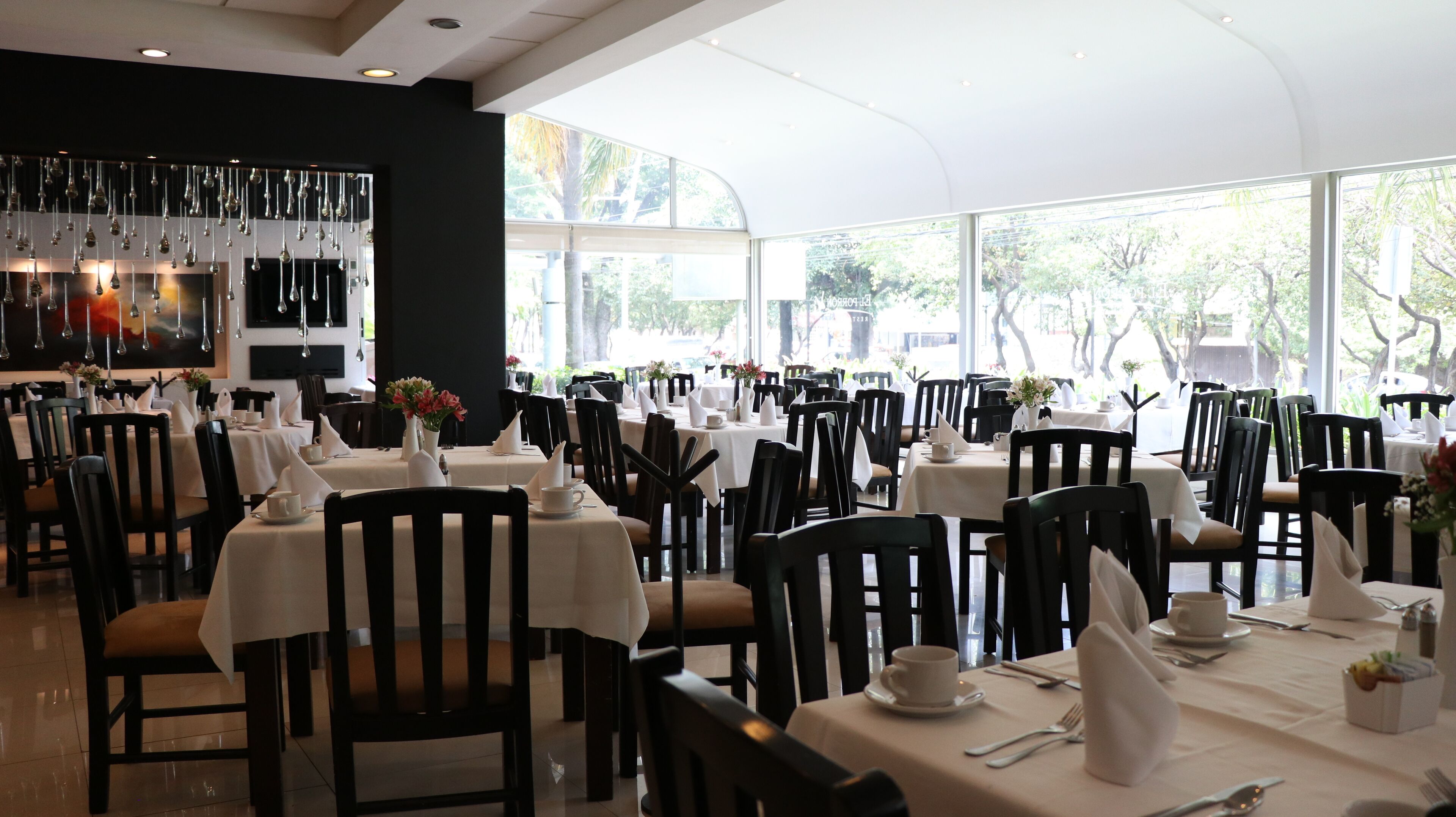 Un restaurante con varias mesas dispuestas para comer, con manteles blancos y sillas negras.