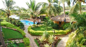 A tropical resort with a swimming pool, palm trees, and a thatched-roof hut. - Santana Beach Resort (Candolim)