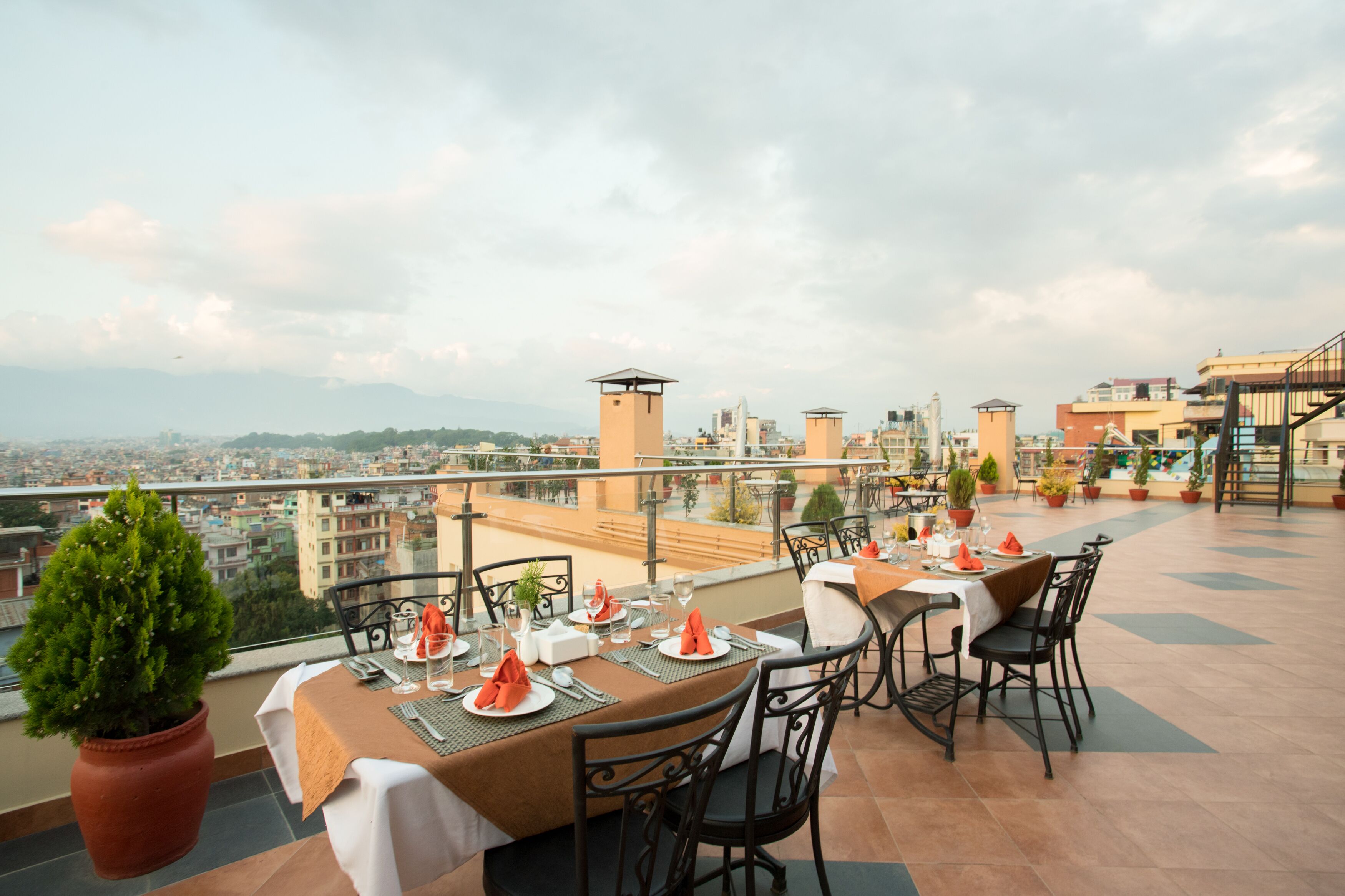 Un restaurante en la azotea con mesas dispuestas para comer, plantas en macetas y vistas a la ciudad.