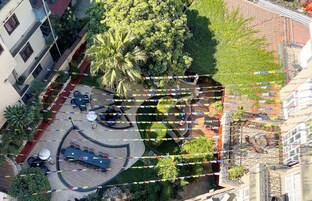 Vista aérea de un patio con mesas al aire libre, rodeado de vegetación y edificios.