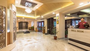 A hotel lobby with a marble floor, a reception desk labeled 'BELL DESK', and a chandelier.