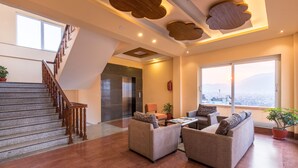 A spacious living area with a staircase, comfortable seating, and large windows offering a view.