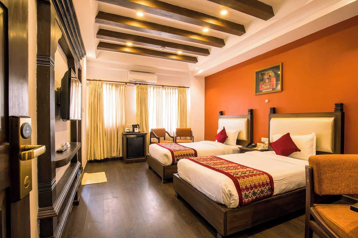 A hotel room with two beds, a desk, chairs, and a television.