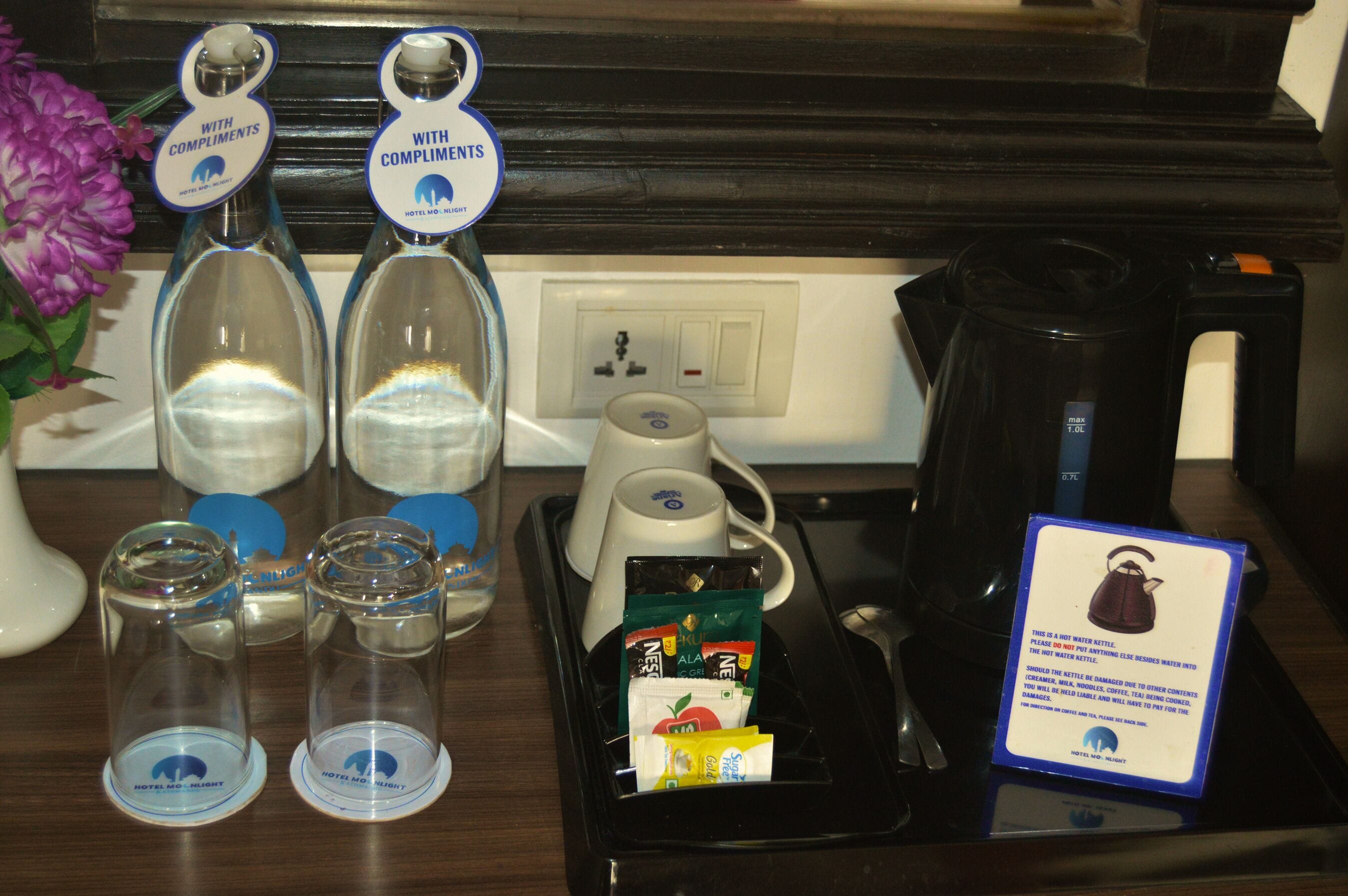 A hotel room's breakfast area with a coffee maker, two glass carafes, a tray with breakfast items, and a sign about the kettle.