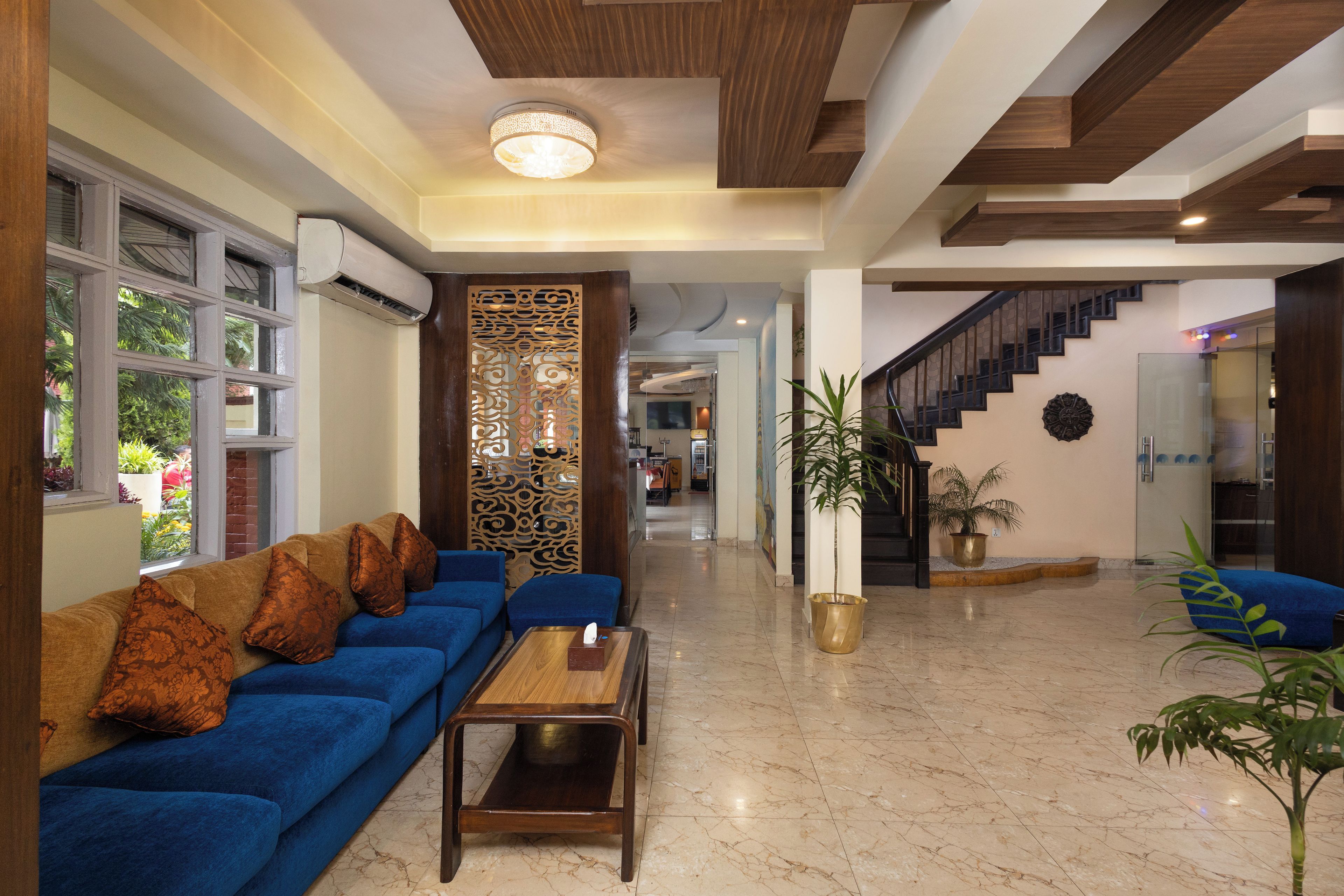 Un hall d’hôtel moderne avec un canapé bleu, une table basse en bois, un paravent décoratif et un escalier.