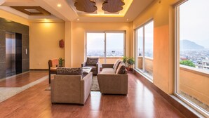 A spacious living area with a modern design, featuring a large window with a city view, a fireplace, and a seating arrangement.