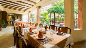 A restaurant with tables set for dining, featuring a view of greenery and brick walls.