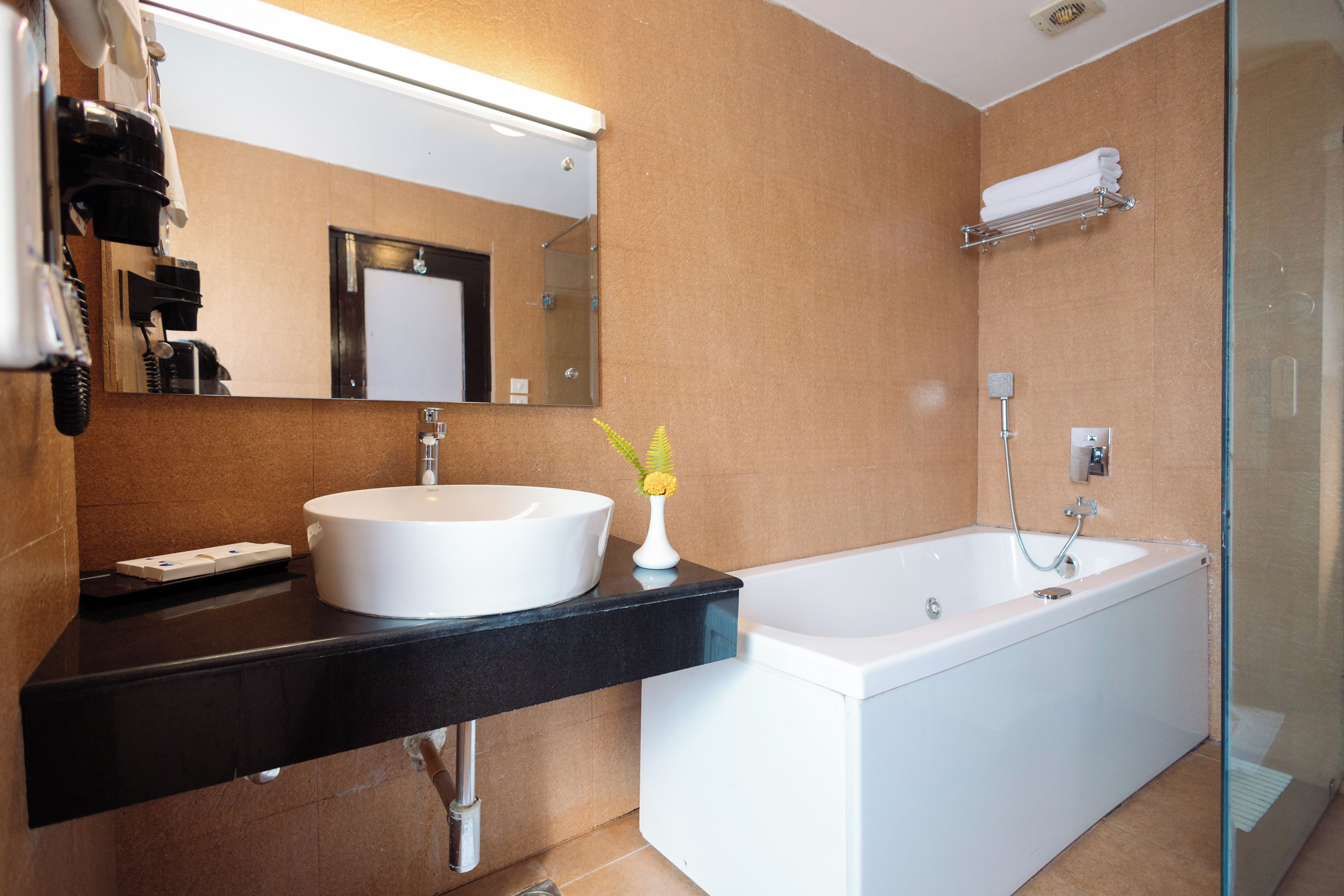 A modern bathroom with a large white sink, a black countertop, a mirror, a white bathtub, and a glass shower enclosure.