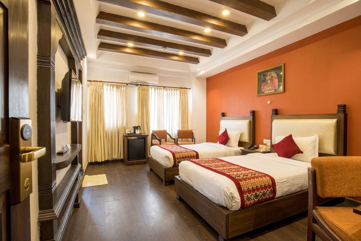 A hotel room with two beds, a desk, a chair, a television, and a painting on the wall.
