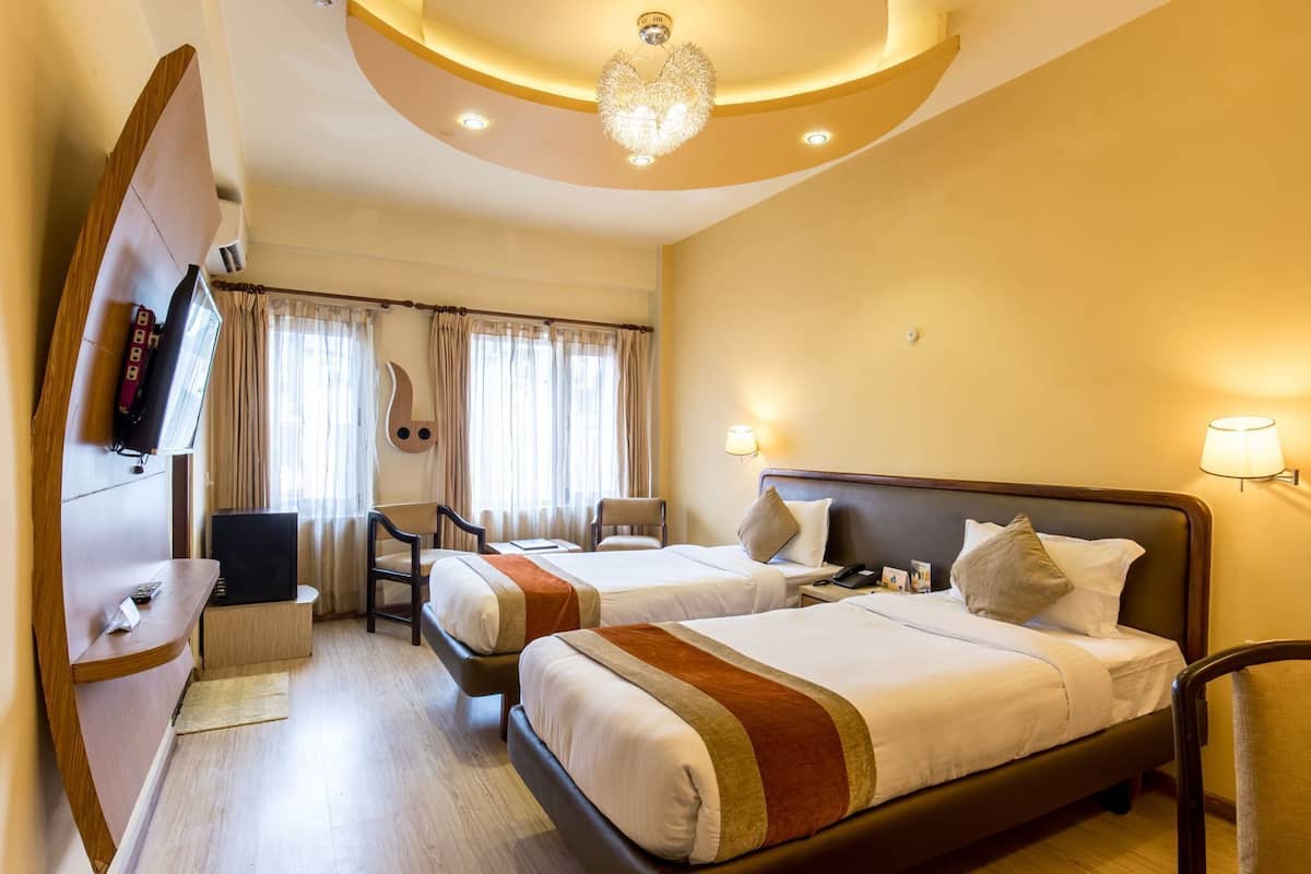 A hotel room with two beds, a TV, a desk, and a chair.