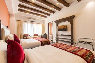 A hotel room with two beds, a wooden ceiling, an air conditioning unit, a television, and a window with curtains.