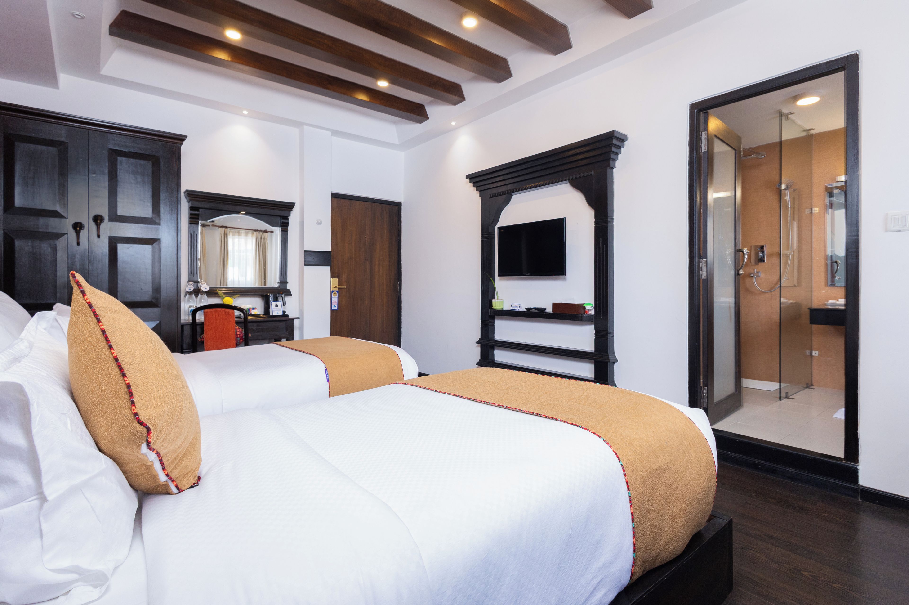 A hotel room with a large bed, a television, a desk with a chair, a mirror, and a sliding door leading to a bathroom.