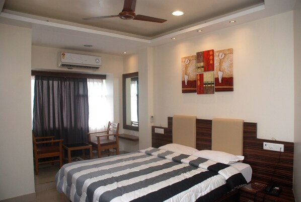 A hotel room with a large bed, a desk, a chair, and a ceiling fan.