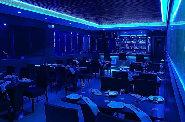 Un restaurante con mesas dispuestas para comer, una zona de bar y un diseño de techo moderno.