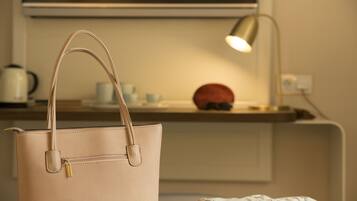 A beige handbag on a bed with a floral blanket, a lamp, and a red object on a bedside table.